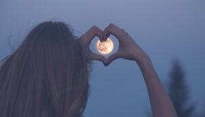 Girl with heart hands over the moon
