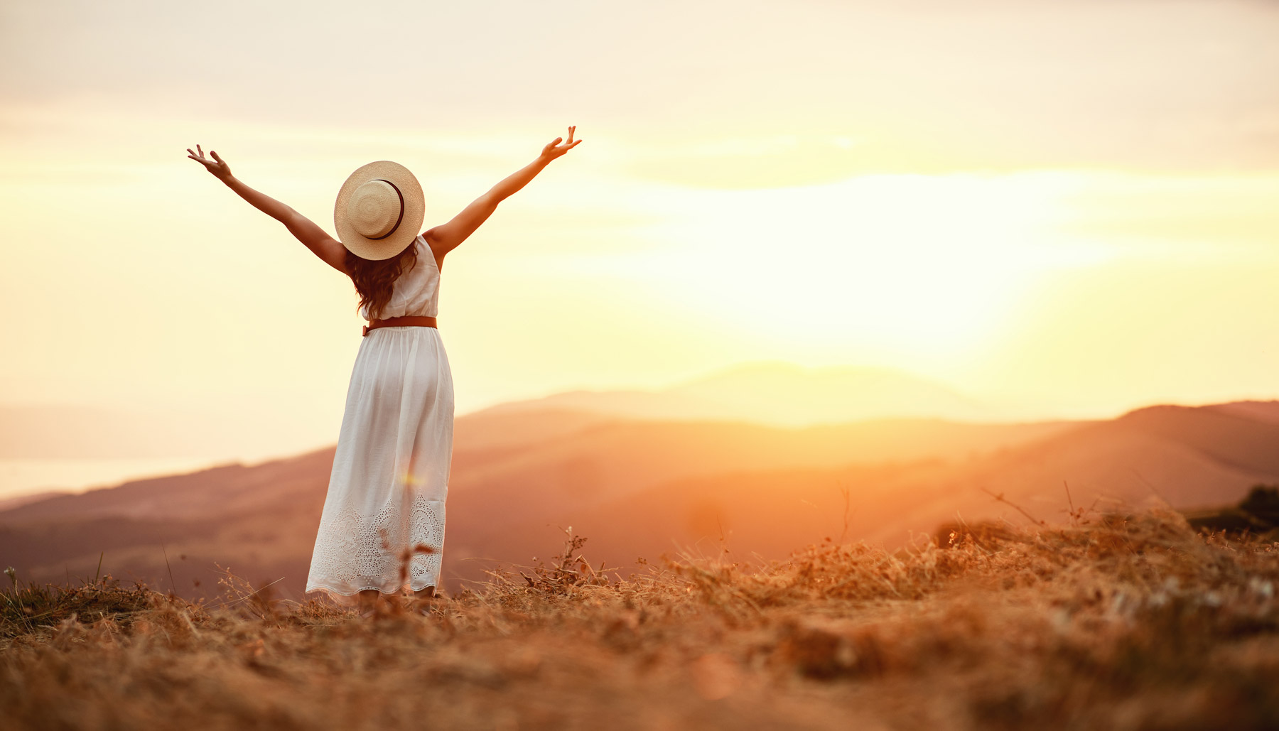 Woman in hat raising arms toward the sun