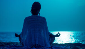 Woman meditating on beach at night